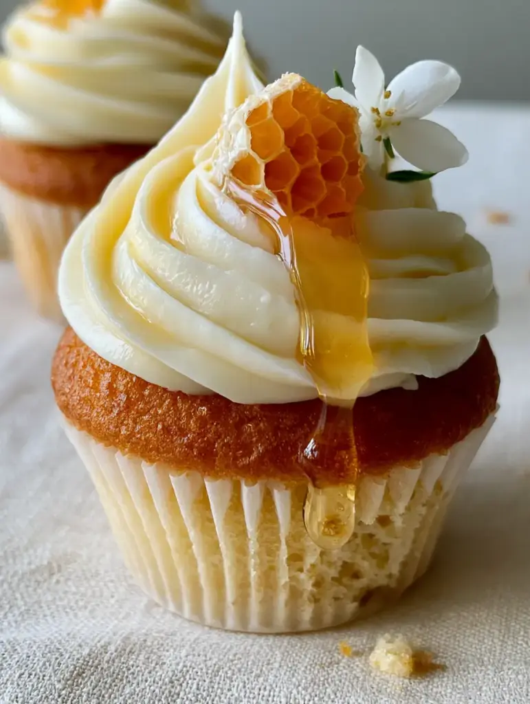 Detail of amber honey drizzle cascading down a tall swirl of ivory buttercream on a honey cupcake.