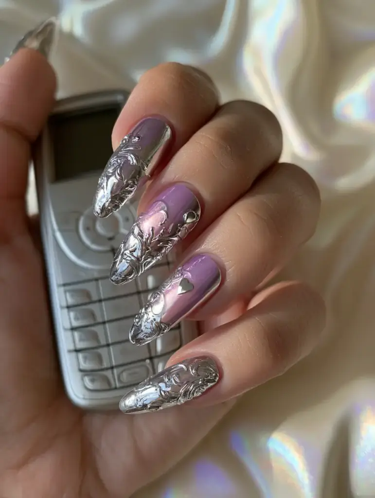 Close up of long almond-shaped nails with metallic silver heart charms and a soft iridescent background.