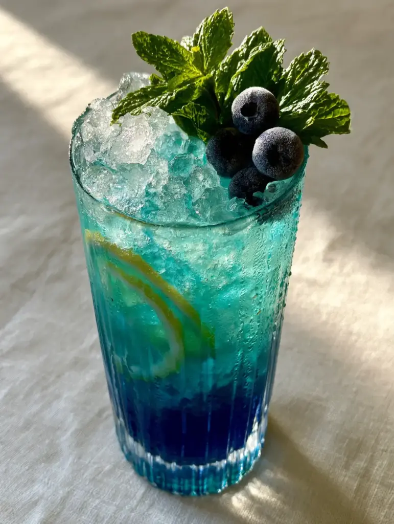 Blue Lemonade Recipe: The Naturally Electric Summer Refresher 1 Top view of Blue Lemonade garnished with a fresh mint sprig and three frosted blueberries on crushed ice.