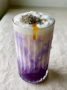 Close-up of a tall ribbed glass with lavender milk tea, showing condensation and white cream marbling down. (lavender milk tea)
