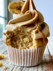 Macro close-up of a Peanut Butter Banana Cupcake with a bite taken out revealing an ultra-fluffy golden-yellow crumb. (Peanut Butter Banana Cupcakes)