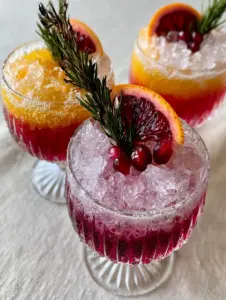 High angle shot of elegant ribbed crystal coupe glasses with sunset-layered non-alcoholic party drinks on a linen cloth.