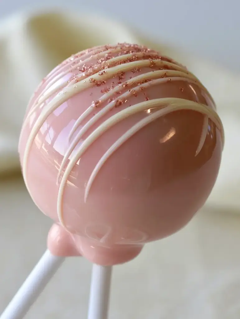 How to Make Cake Pops: The Ultimate Professional Guide to Glossy Pink Treats 1 Close up of the white chocolate drizzle and microscopic rose-gold sugar crystals on a smooth pink candy coating.