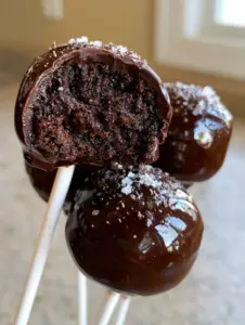 A smartphone photo of three gourmet Chocolate cake pops; one has a bite taken out revealing a dense, fudgy interior with no crumbs. (Chocolate cake pops)