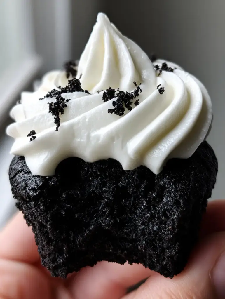 black velvet cupcakes with thick cream cheese frosting 1 A close-up of black velvet cupcakes featuring sharp white frosting ridges and scattered black cocoa crumbs.