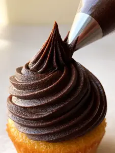 Close-up of a metal star tip piping thick chocolate buttercream frosting with matte fudgy texture.
