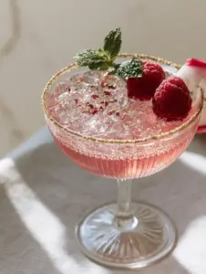 A close up of a pink mocktail in a ribbed glass showing effervescent bubbles and gold sugar rim. (Bridal Shower Mocktails)
